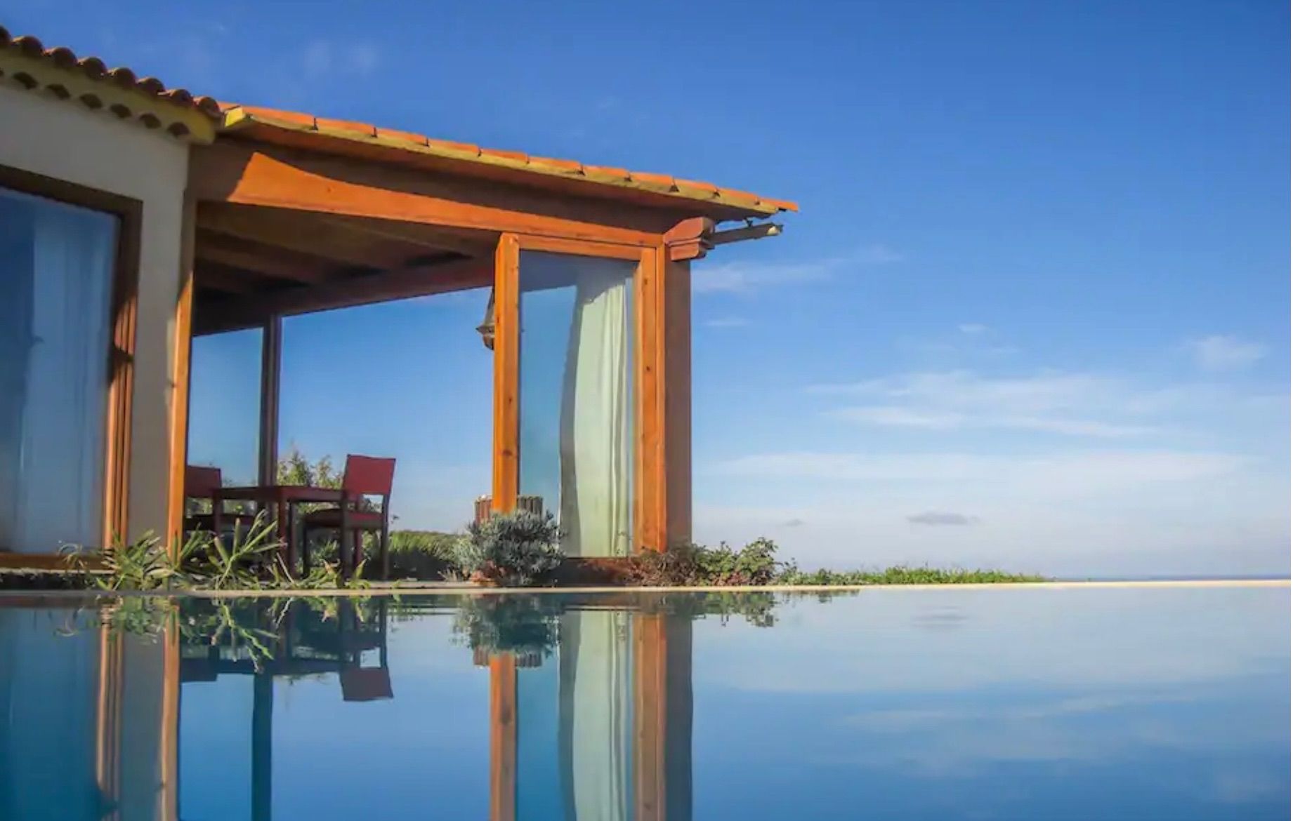 Bellamare: Infinity-Pool, in dem sich der Wintergarten mit Holzrahmen und der blaue Himmel spiegeln