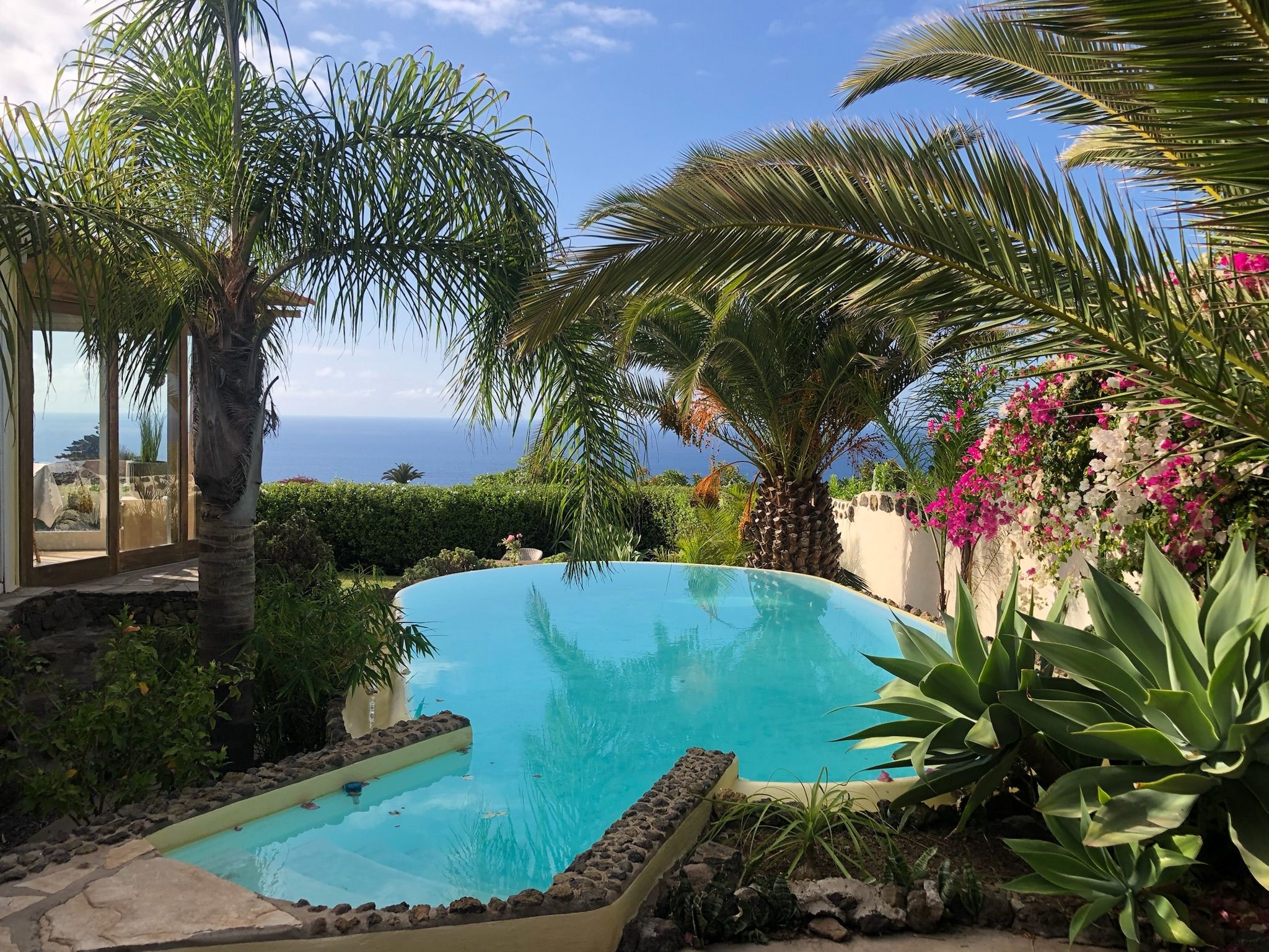 Bellamare: Pool zwischen Palmen, Agaven und Bougainvillea, dahinter Blick auf den Atlantik