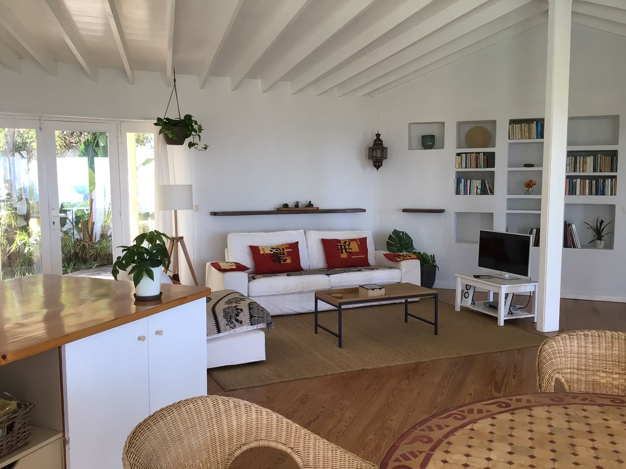 Bellamare: Wohnbereich mit weißem Sofa, Couchtisch, Fernseher und Bücherregalen unter offener Balkendecke