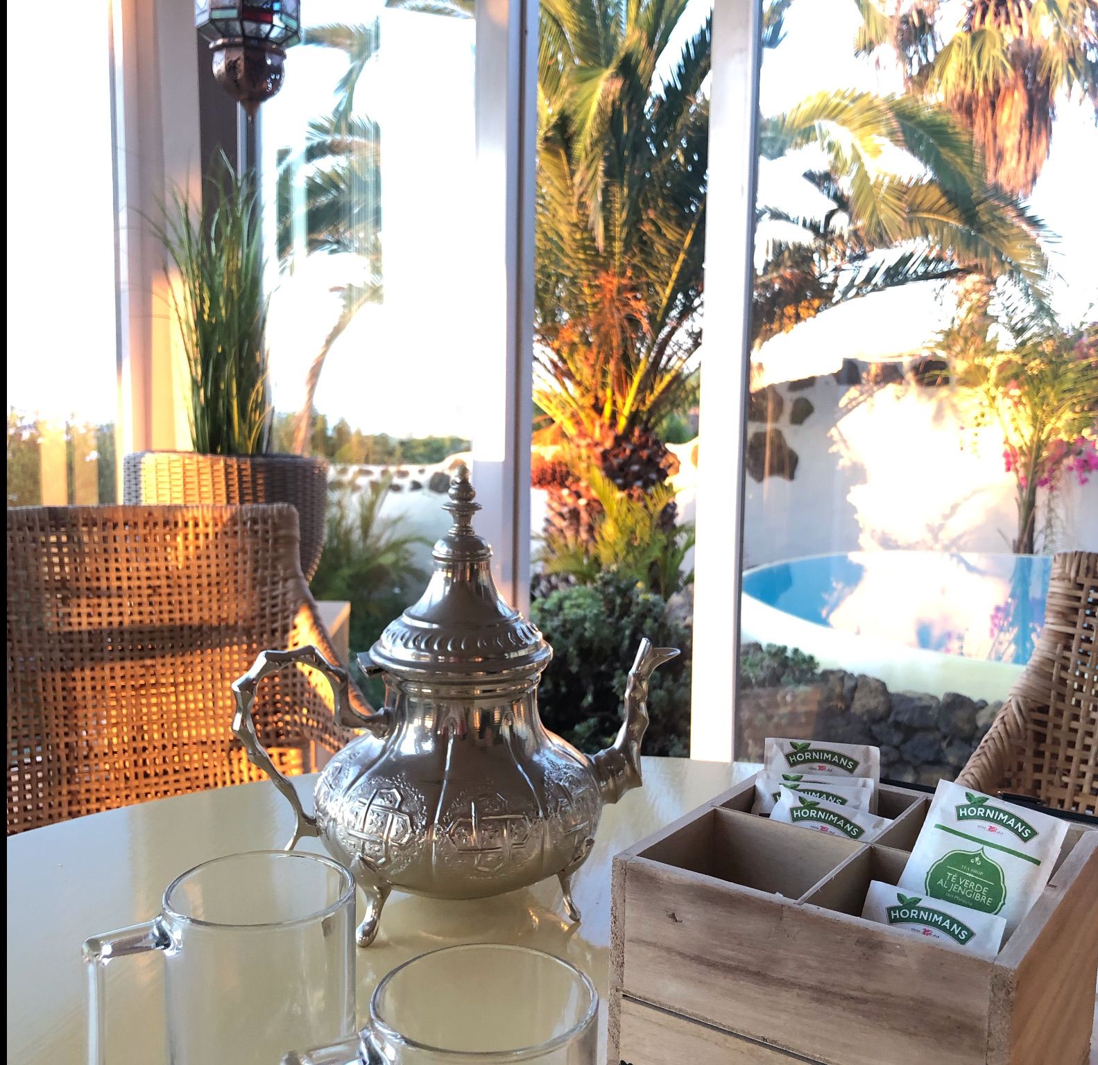 Bellamare: Marokkanische Teekanne und Teegläser auf einem Tisch, durch das Fenster Blick auf Pool und Palmen