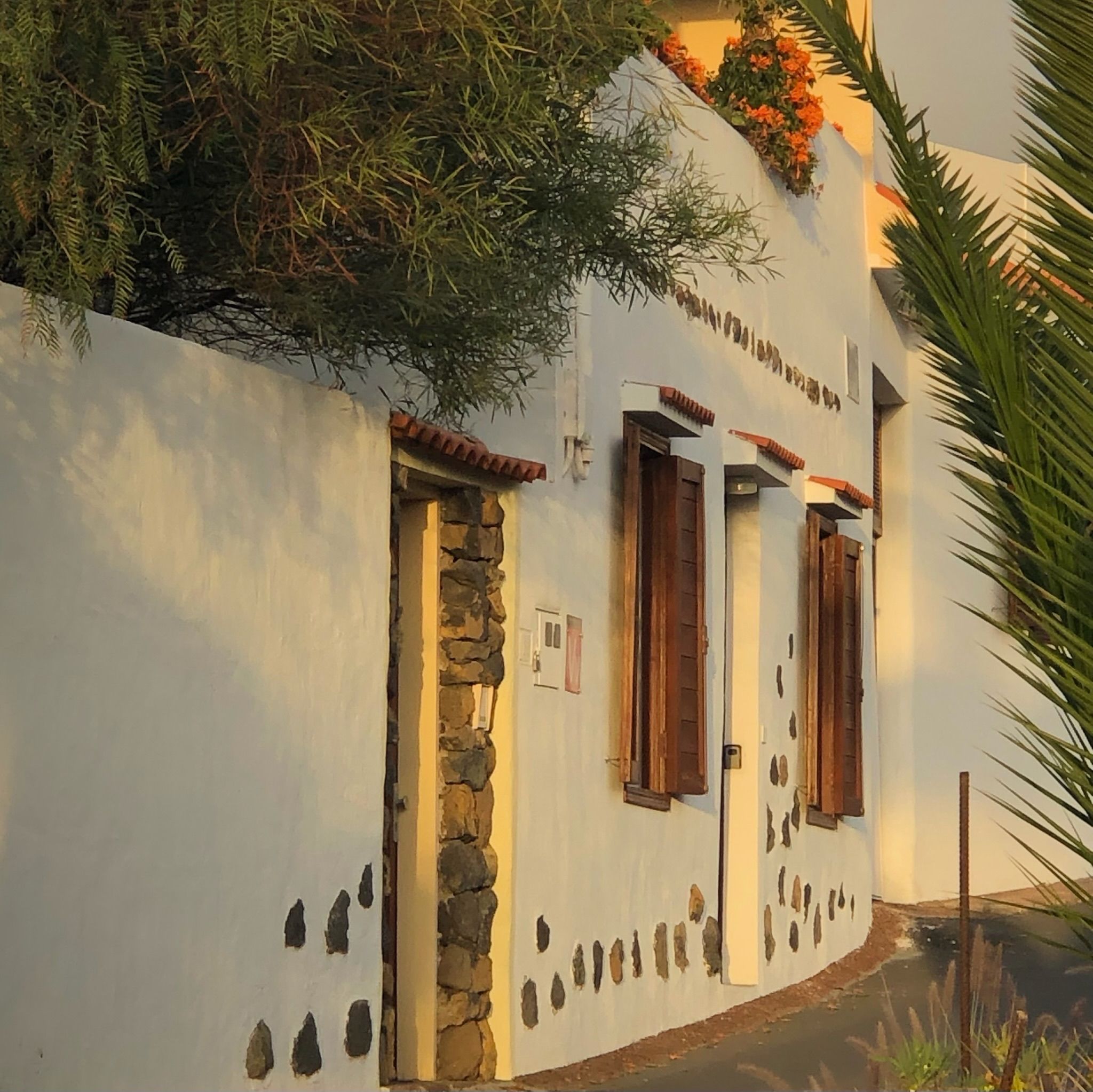 Casita Aquavista: Weiße Hausfassade mit Natursteinelementen und Holzfensterläden im warmen Abendlicht