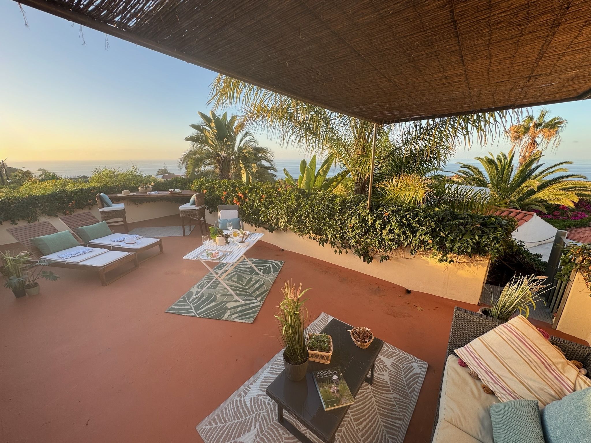 Casita Aquavista: Dachterrasse mit Sonnenliegen, Sofa und Essplatz unter Schilfdach, Blick auf das Meer im Abendlicht